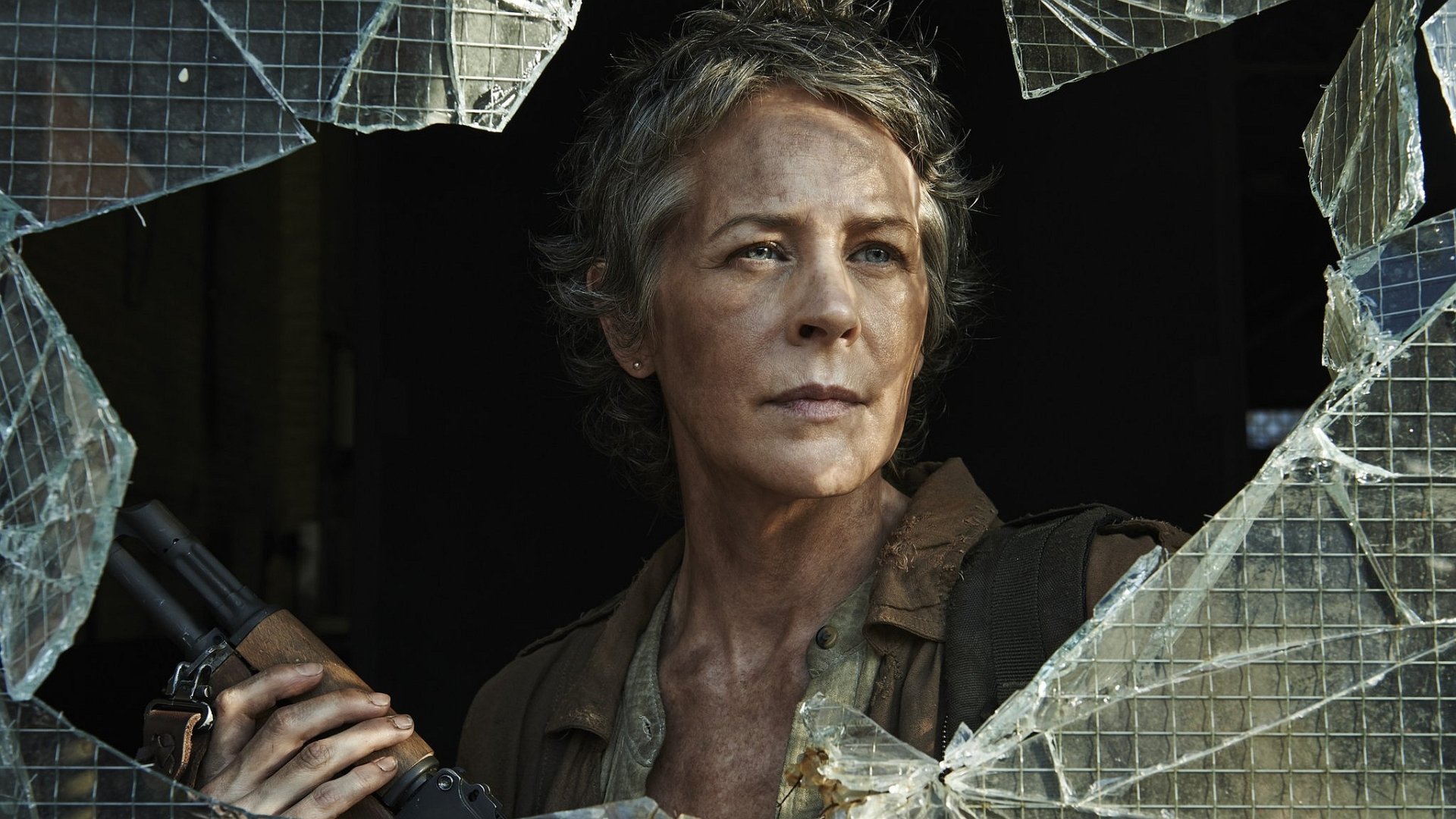A dramatic HD wallpaper from *The Walking Dead*, featuring a determined character peering through a shattered window, holding a weapon amidst a tense atmosphere.