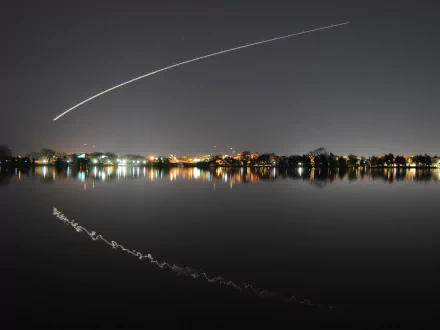 Night photography of a city skyline with an arcing light streak and its reflection across calm water — HD PC desktop wallpaper and background.