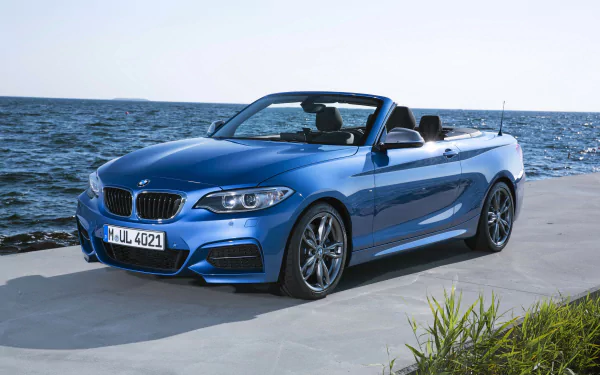 A blue BMW M235i convertible parked by the sea, captured in a crisp 4K Ultra HD wallpaper showcasing the vehicle's sleek design and sporty elegance.