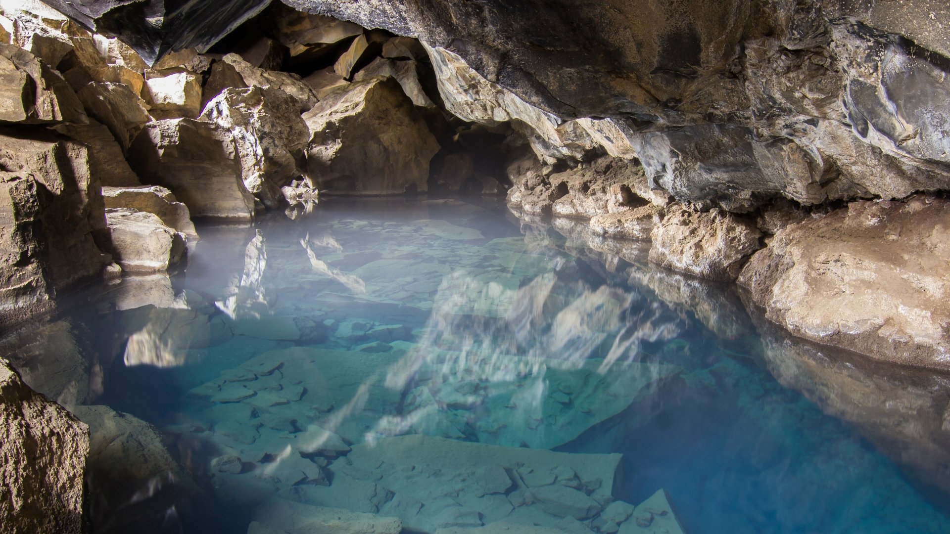 4K Ultra HD PC desktop wallpaper — crystal-clear blue water in a rocky cave pool, sunlight reflecting on limestone walls.