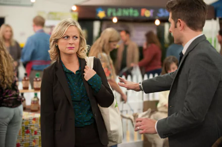 HD wallpaper featuring a scene from Parks and Recreation with two characters conversing at an indoor event.