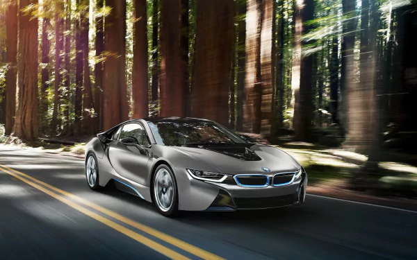 A silver BMW i8 sports car drives along a two-lane road surrounded by tall forest trees, captured in HD for a PC desktop wallpaper.