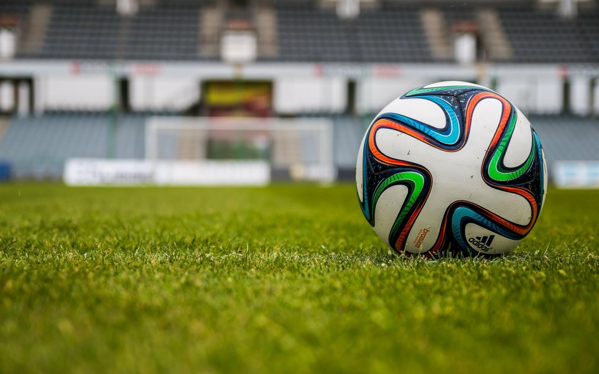 HD PC desktop wallpaper featuring a colorful soccer ball resting on green grass in a stadium, capturing the essence of soccer and sports action.