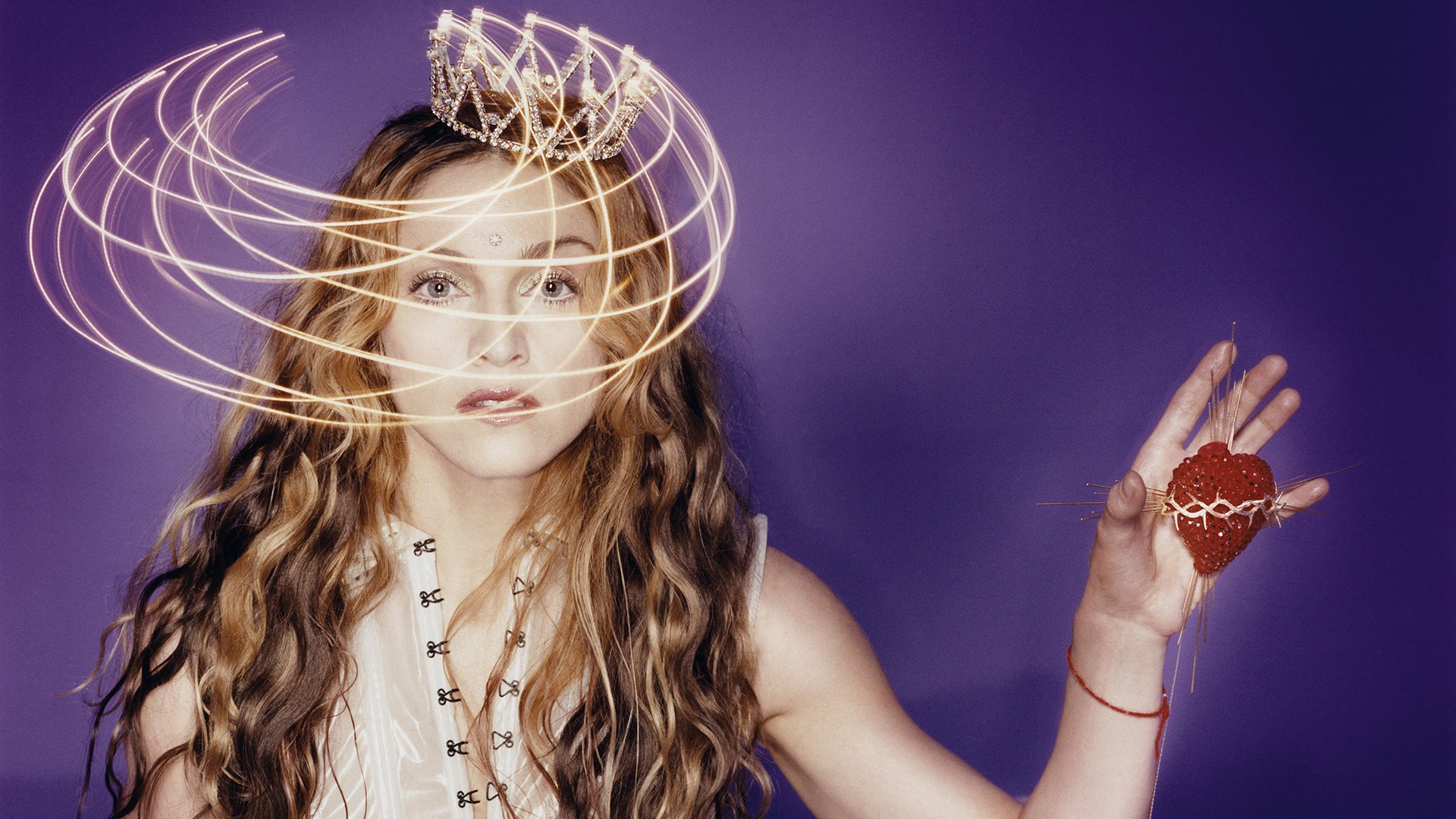 HD PC desktop wallpaper featuring Madonna against a purple background, with artistic light swirls around her head and a heart-shaped ornament in her hand, highlighting music and style.
