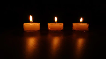 A 4K Ultra HD photograph of three lit candles in a row against a dark background, creating a warm, reflective glow on the surface beneath them.