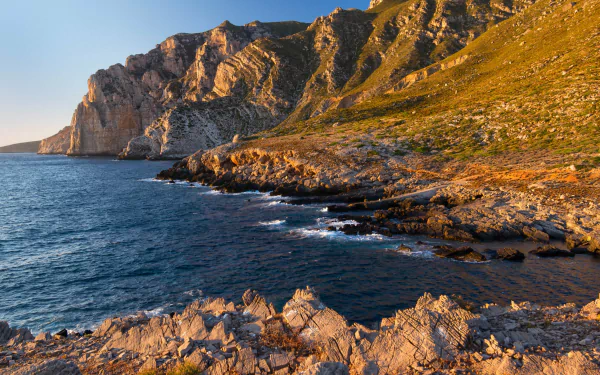 4K Ultra HD desktop wallpaper depicting a rugged cliff bathed in warm sunlight, overlooking a calm ocean under a clear blue sky.