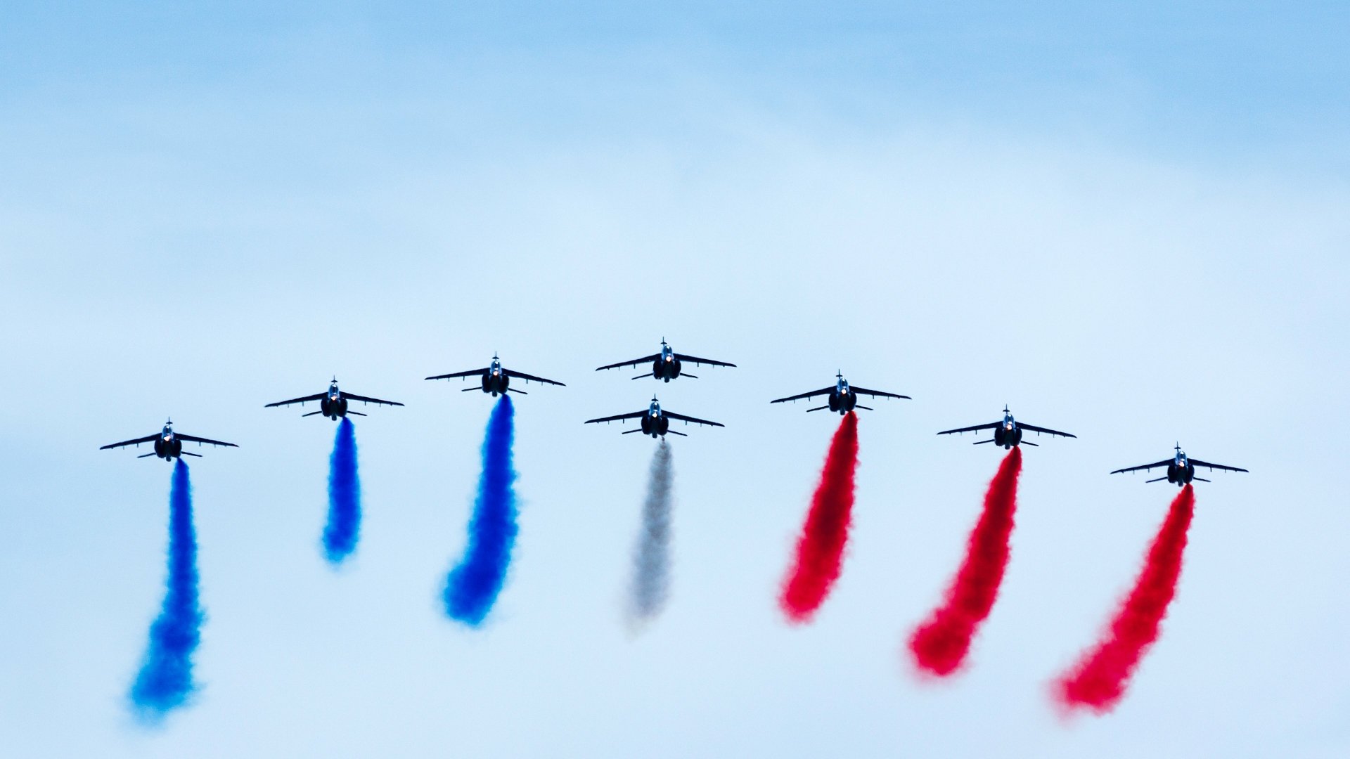 A formation of military airplanes performing an air show, emitting blue, black, and red smoke trails against a clear sky in 4K Ultra HD quality.