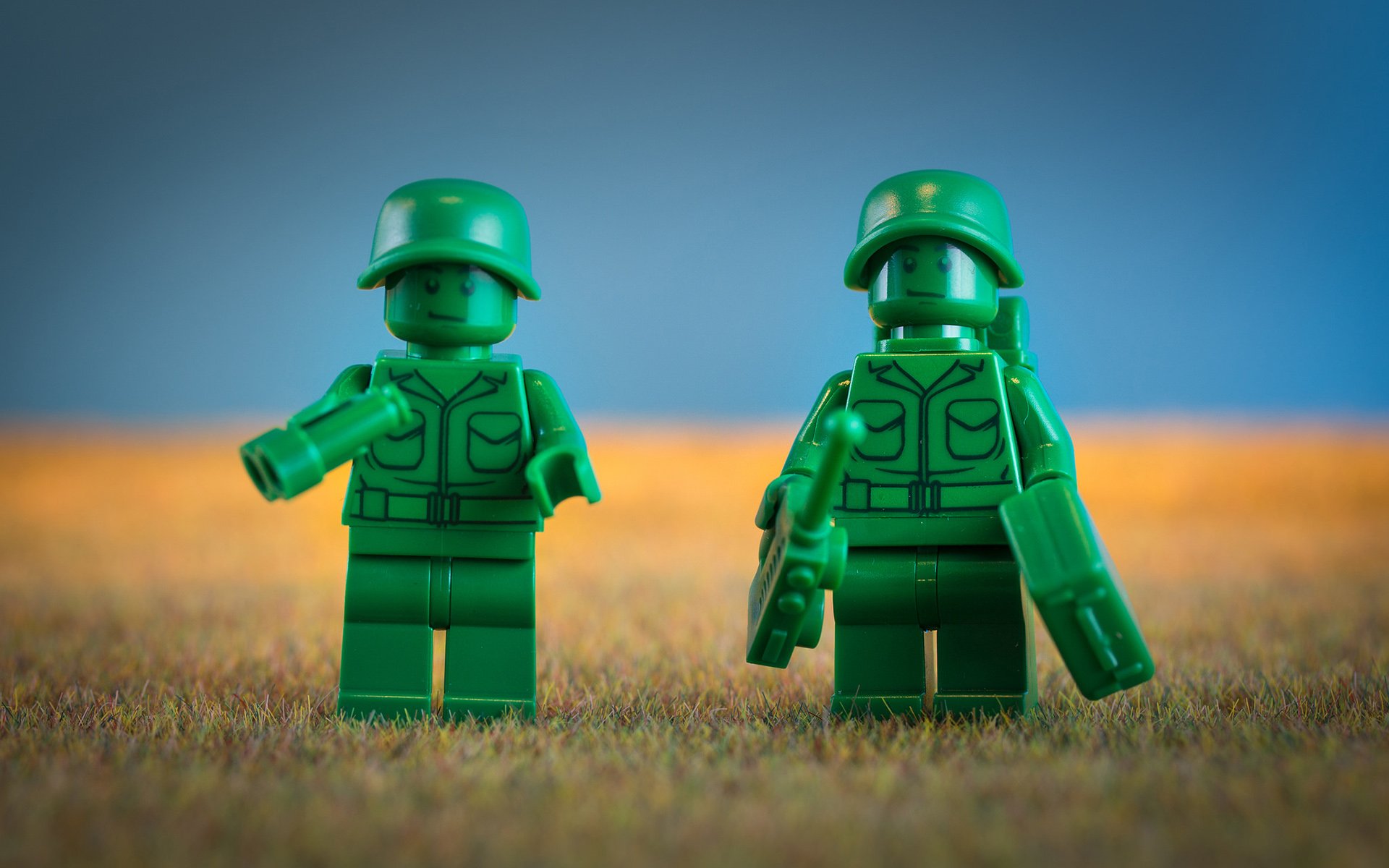 HD PC desktop wallpaper featuring two green LEGO soldiers standing on a textured surface with a blurred background, showcasing man-made toy figures.