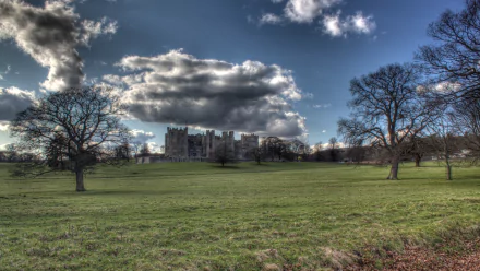 HD PC desktop wallpaper featuring the man-made structure of Raby Castle under a dramatic sky, framed by trees on a vast green lawn.