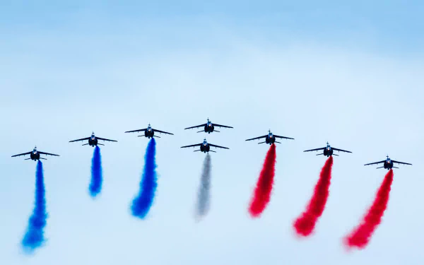 A formation of military airplanes performing an air show, emitting blue, black, and red smoke trails against a clear sky in 4K Ultra HD quality.