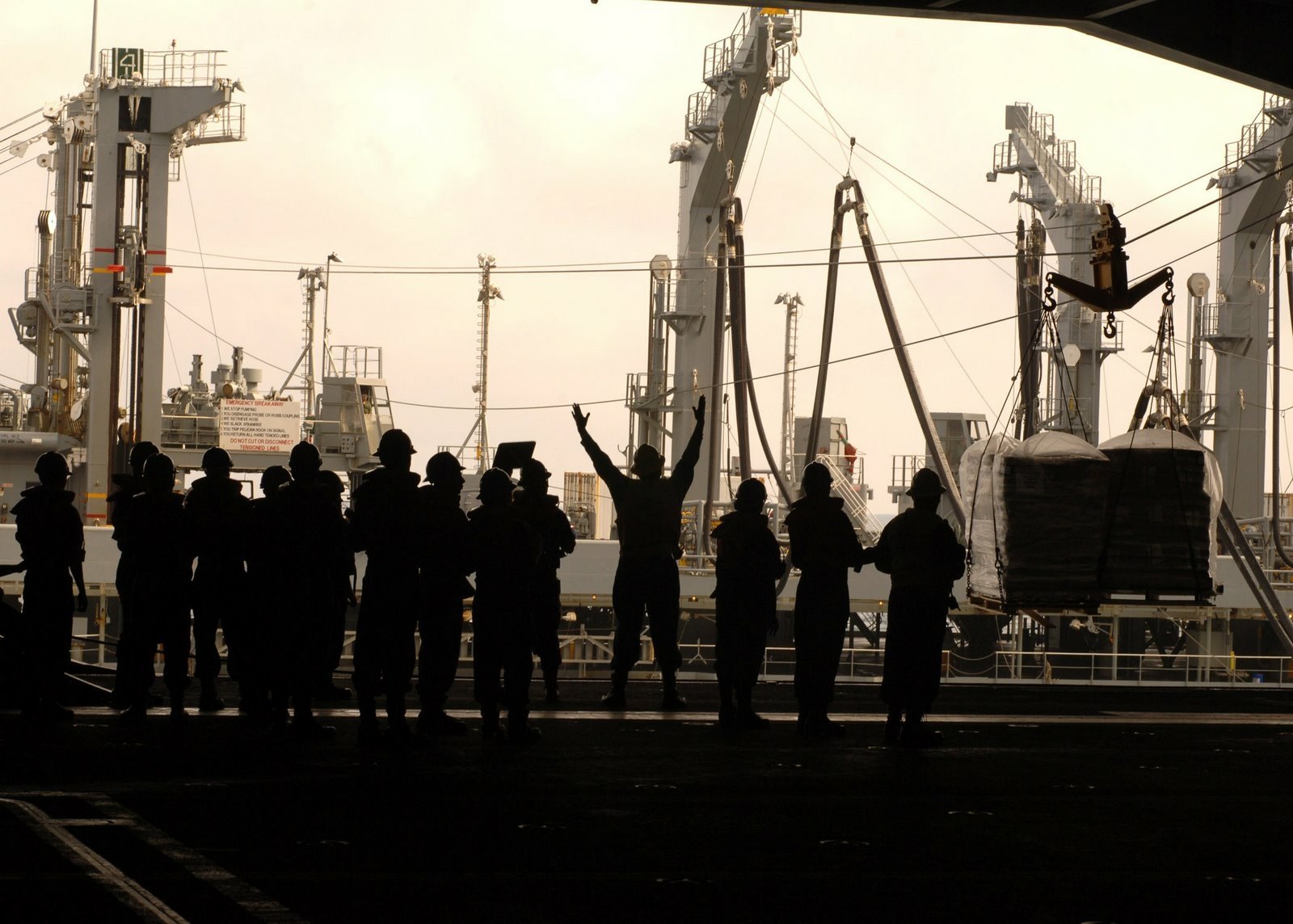 Silhouetted crew members on the deck of the USS George Washington (CVN-73) aircraft carrier, with cranes and naval equipment visible in the background.