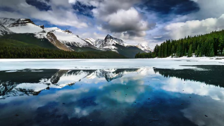 4K Ultra HD desktop wallpaper featuring snow-capped mountains and dense forest reflected vividly in a calm lake under a dramatic cloudy sky.