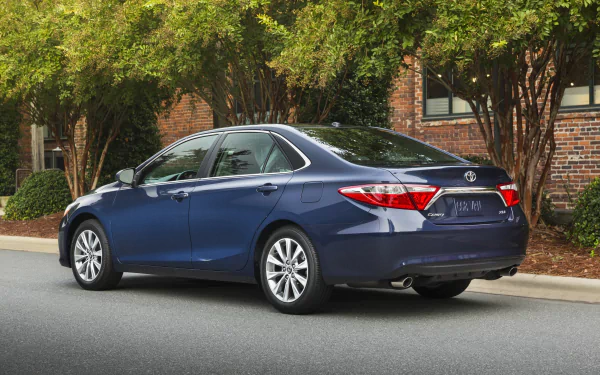 Blue Toyota Camry XLE sedan parked beside a brick building — 4K Ultra HD PC desktop wallpaper/background, rear three-quarter view.