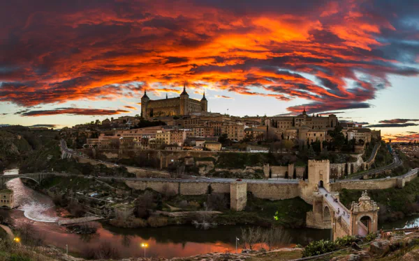 Sunset over the historic man-made cityscape of Toledo, Spain, with vibrant orange clouds illuminating the skyline in this HD desktop wallpaper.