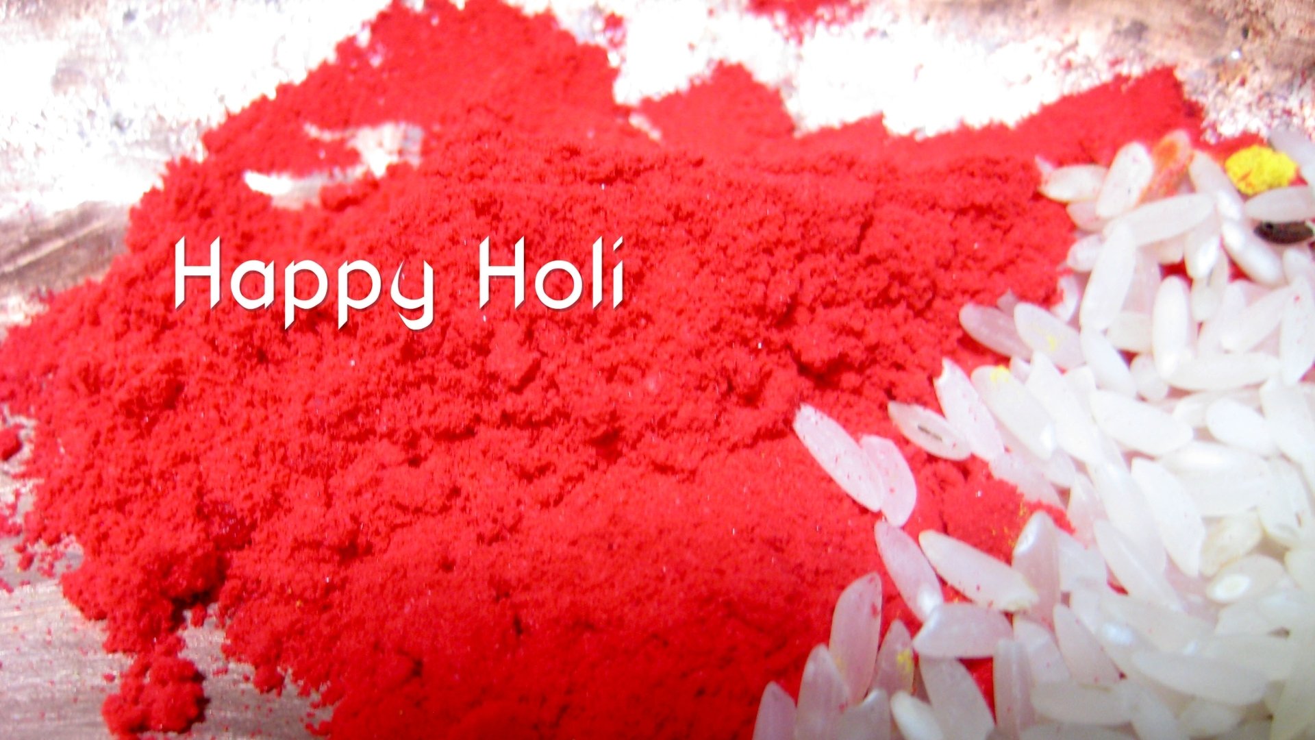 HD PC desktop wallpaper showing vivid red Holi gulal powder and white rice grains with 'Happy Holi' text — colorful holiday background