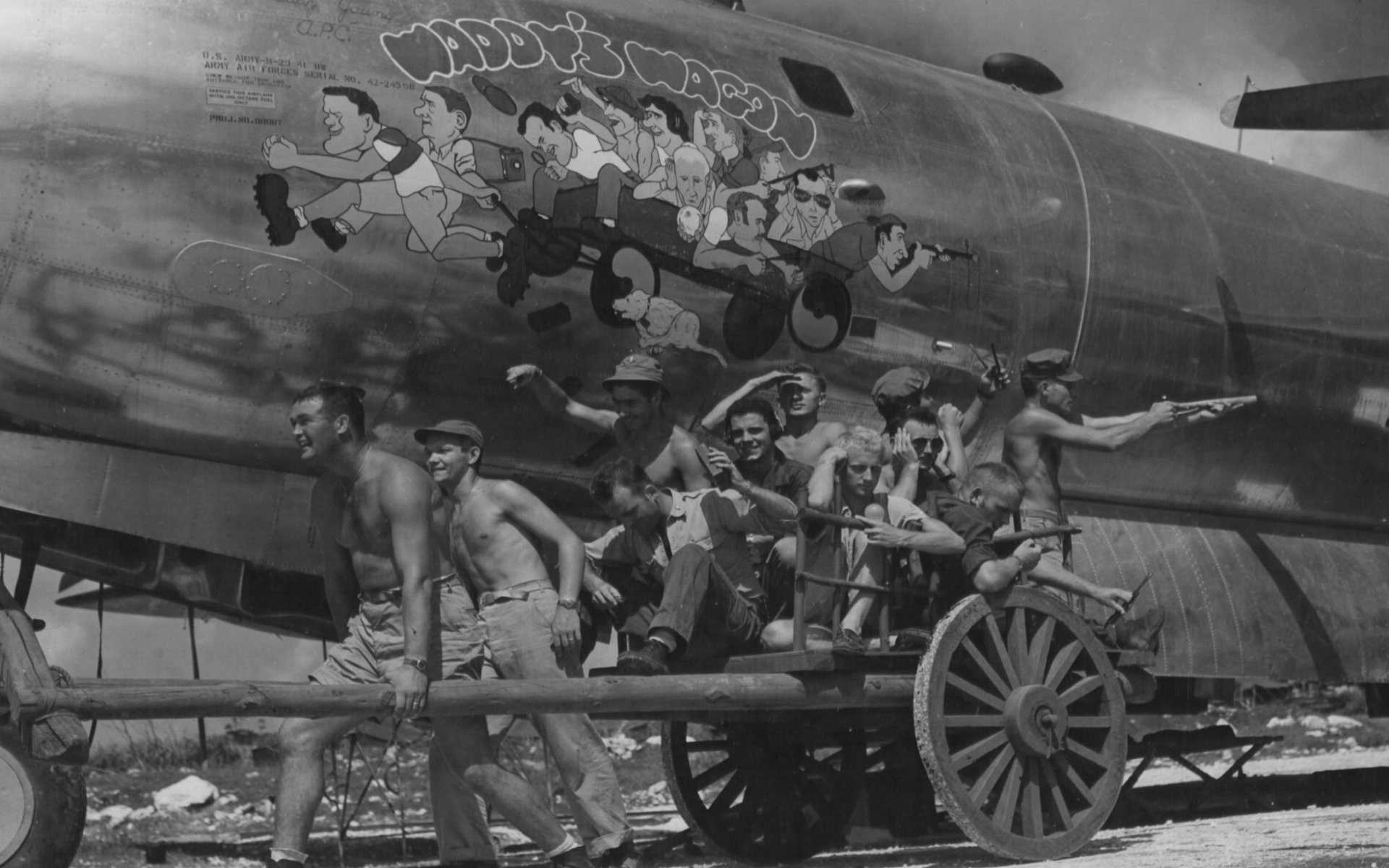 Black-and-white military photo showing servicemen pulling a cart in front of an aircraft decorated with colorful nose art; HD PC desktop wallpaper background.