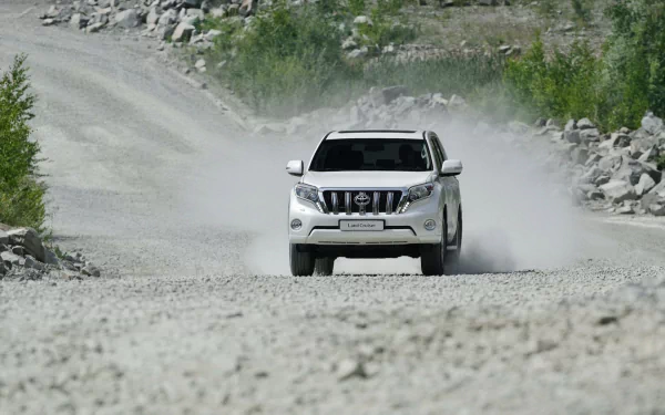A Toyota Land Cruiser Prado drives through a dusty, rocky terrain, showcasing its rugged design and off-road capabilities in this HD PC desktop wallpaper.