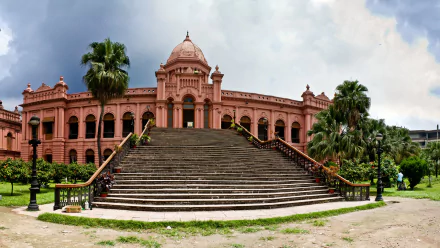 HD PC desktop wallpaper background of Ahsan Manzil: a grand pink man-made palace with wide stone steps, flanked by palm trees beneath a dramatic cloudy sky.