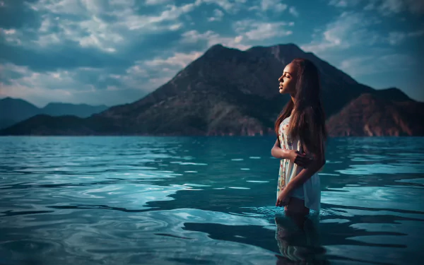 A woman stands in serene blue waters with a mountainous backdrop in Turkey, creating a captivating scene. This HD desktop wallpaper and background image features a model named Mary Senn.