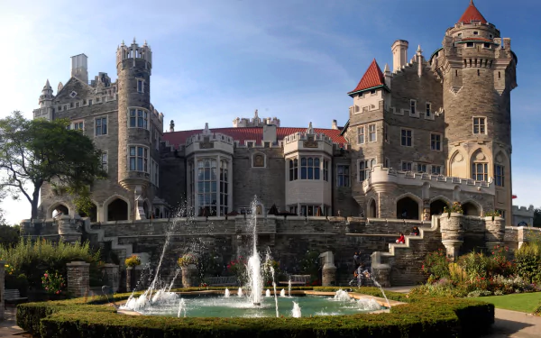 Casa Loma, a man-made historic castle with turrets and towers, stands against a blue sky with a fountain and garden in the foreground, HD desktop wallpaper.
