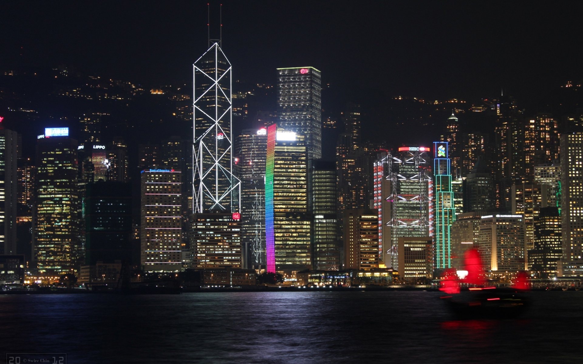 Night view of Hong Kong’s illuminated skyline with iconic skyscrapers and a traditional red-sailed boat on the water, captured in 4K Ultra HD.