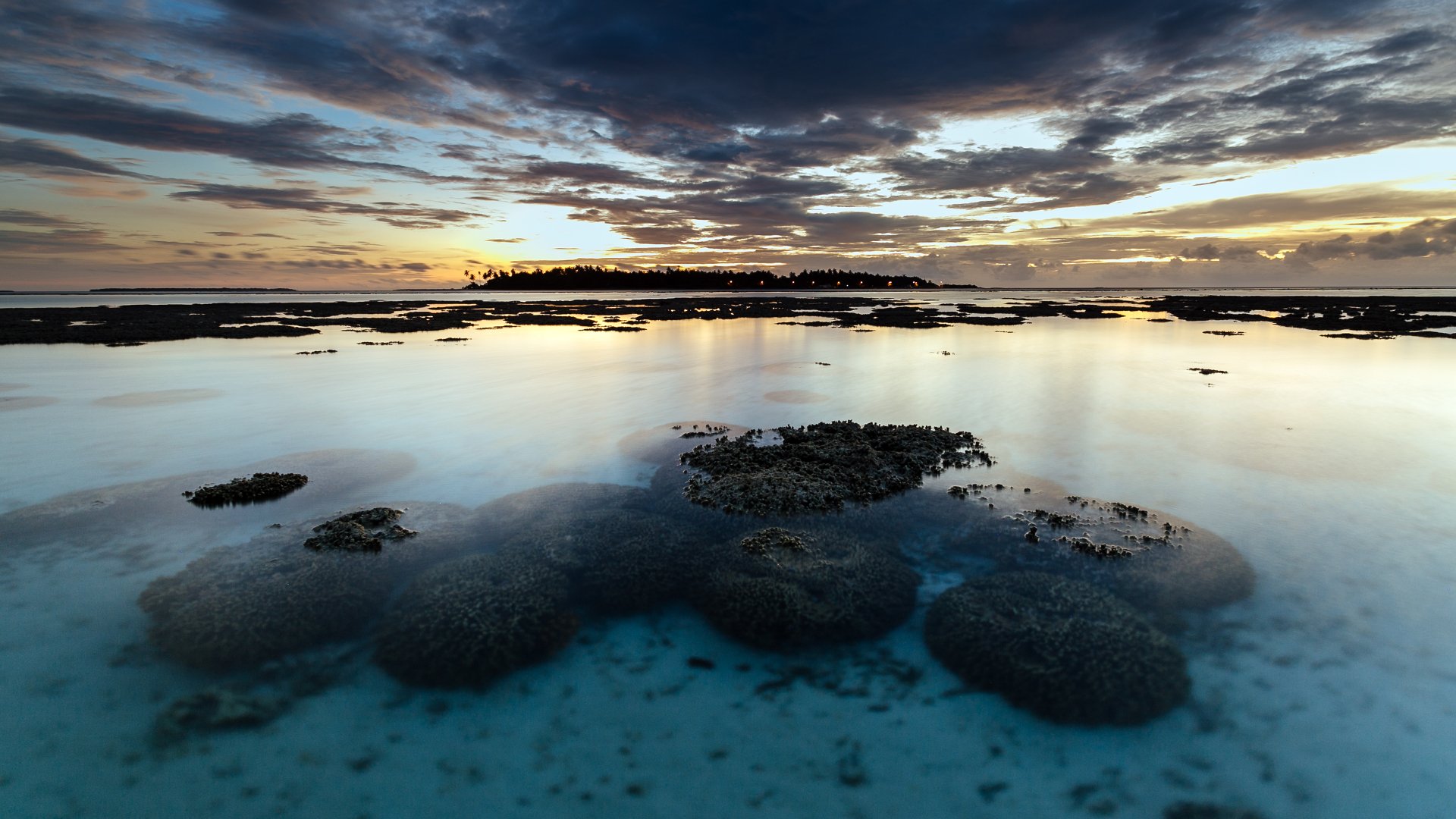 4K Ultra HD nature landscape: tranquil coastal reef and calm turquoise waters at sunset, distant island silhouette under a dramatic cloudscape — PC desktop wallpaper and background.