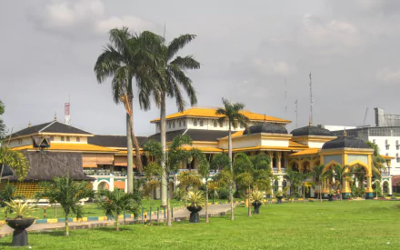 HD PC desktop wallpaper of Maimun Palace — a man-made yellow palace framed by palm trees and a green lawn beneath a cloudy sky.