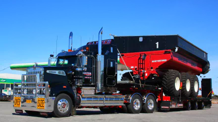 HD desktop wallpaper of a black Kenworth truck hauling a large red agricultural trailer against a clear blue sky.