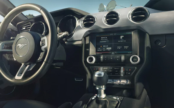 A detailed view of the interior of a 2015 Ford Mustang GT, featuring the steering wheel, dashboard, and climate controls, with sunglasses resting on the dashboard.
