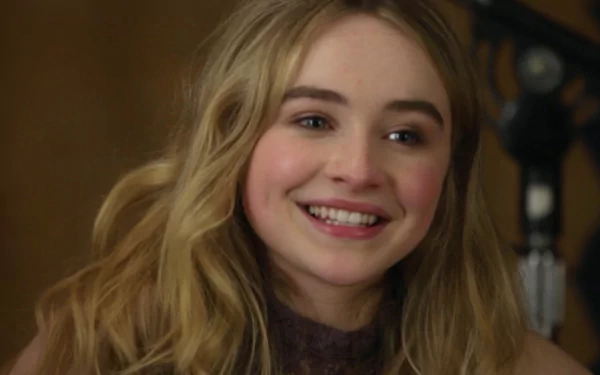 A high-definition wallpaper featuring Sabrina Carpenter smiling, capturing her vibrant personality against a softly blurred background.