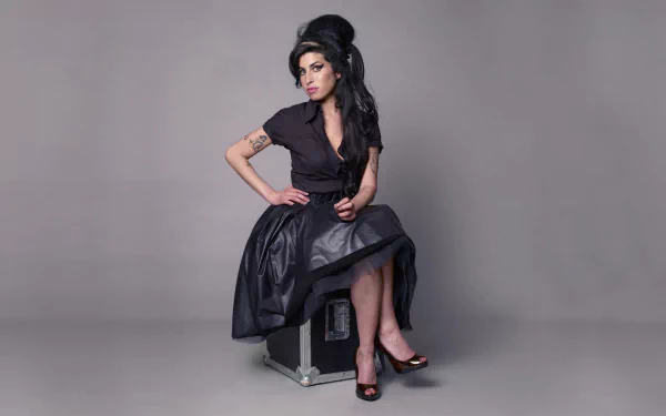 HD desktop wallpaper featuring English singer Amy Winehouse in a black dress, showcasing her signature beehive hairstyle and tattoos against a plain gray background.