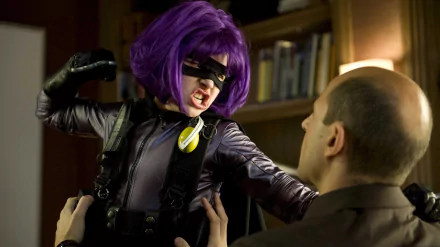 Hit-Girl from the movie Kick-Ass, portrayed by Chloë Grace Moretz, fiercely confronts a man, showcasing her iconic purple wig and striking costume in this HD desktop wallpaper.