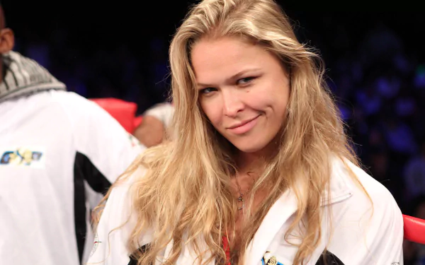 Ronda Rousey confidently smiles in a sports setting, showcasing her dynamic presence. This HD image serves as an engaging desktop wallpaper for sports enthusiasts.