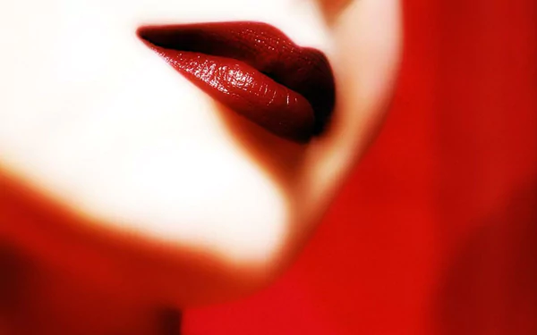 A close-up of a woman's lips adorned with rich red lipstick, featuring a blurred background in shades of red, creating an elegant and striking HD desktop wallpaper.