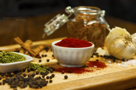 Macro shot of colorful herbs and spices including red chili powder, black pepper, cinnamon sticks, and garlic on a wooden board, captured in 4K Ultra HD for PC wallpaper.