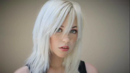 A close-up of a woman with white hair and freckles, featuring striking green eyes. This HD wallpaper showcases her captivating expression against a soft background.