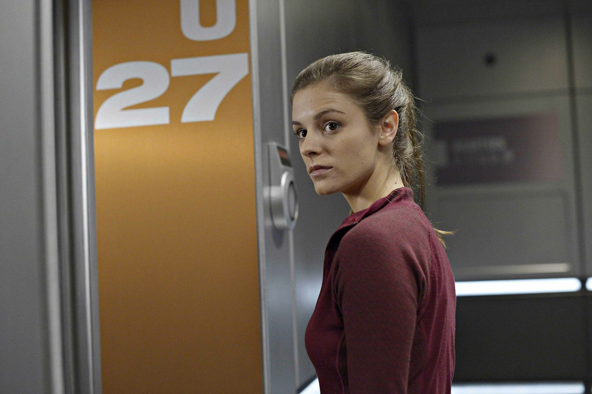 HD wallpaper featuring a woman from the TV show Helix, standing by a door marked with the number 27, suitable as a desktop background.
