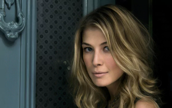 HD desktop wallpaper featuring Rosamund Pike with a captivating gaze against a muted blue door background.
