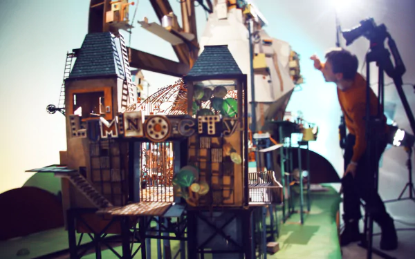 HD desktop wallpaper of Lumino City with a detailed model of a whimsical building and a person setting up the scene in the background.