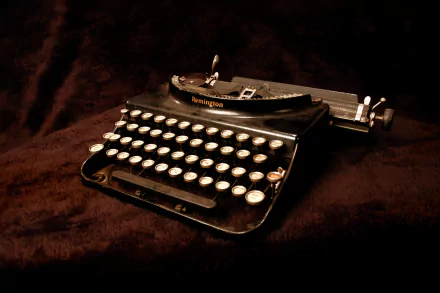 HD desktop wallpaper of a vintage black typewriter on a dark textured surface, showcasing its classic man-made design and keys in sharp detail.