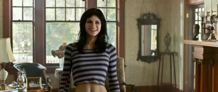 Alexandra Daddario in a scene from *Texas Chainsaw 3D*, smiling while wearing a striped crop top, set in a sunlit room with vintage decor. HD wallpaper background.