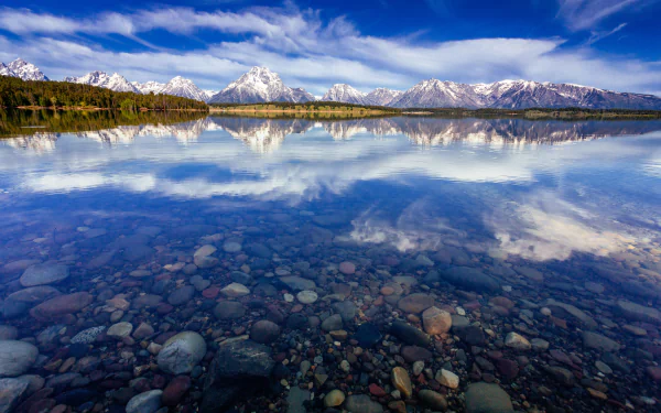 Crystal-clear waters of Jackson Lake reflect the snow-capped Mount Moran and Grand Teton peaks in Wyoming’s Grand Teton National Park under a vibrant blue sky.