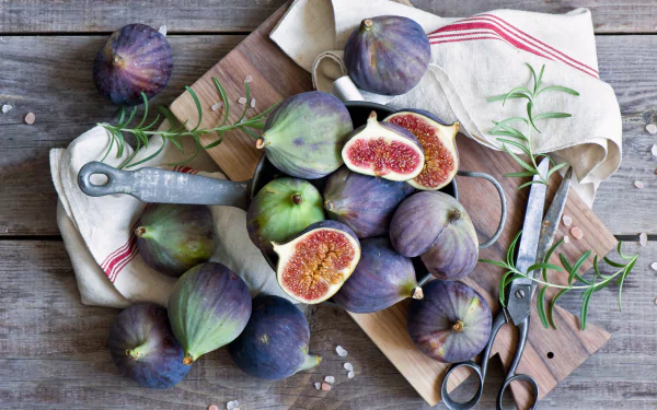 HD PC desktop wallpaper featuring fresh figs, some whole and some halved, arranged on a wooden cutting board with rosemary sprigs and kitchen tools.