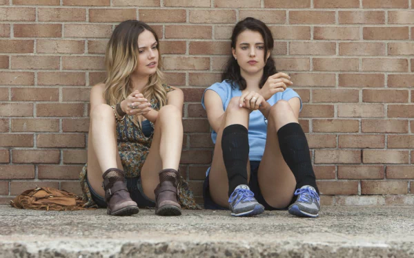 HD desktop wallpaper featuring two young women sitting against a brick wall, from the TV show The Leftovers.