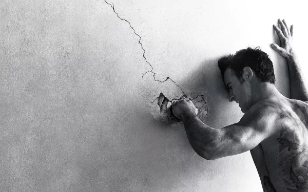 Black and white HD desktop wallpaper from the TV show The Leftovers, featuring a shirtless man punching a cracked wall with intense emotion.