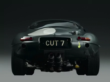Rear view of a classic Jaguar E-Type displayed as an HD PC desktop wallpaper with a dark background, highlighting its sleek vintage design and racing details.