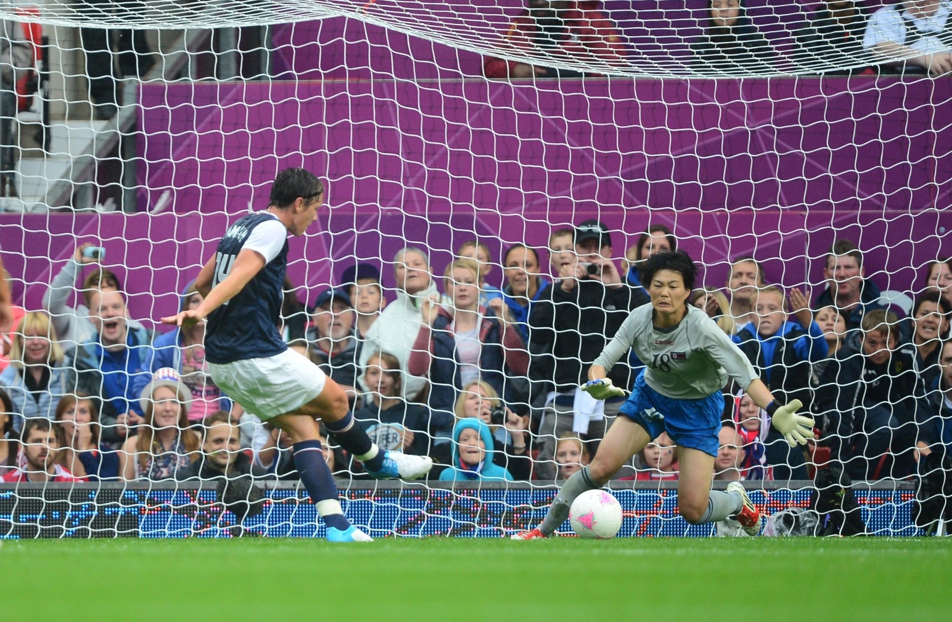 A soccer match captured in vibrant 4K Ultra HD, showcasing a player taking a decisive shot on goal as the goalkeeper prepares for defense amidst an engaged crowd.