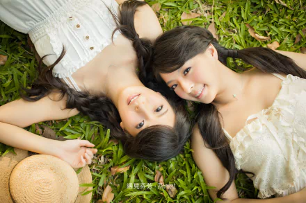 Two women with braids and smiles lie on the grass, creating a serene and joyful HD desktop wallpaper and background.