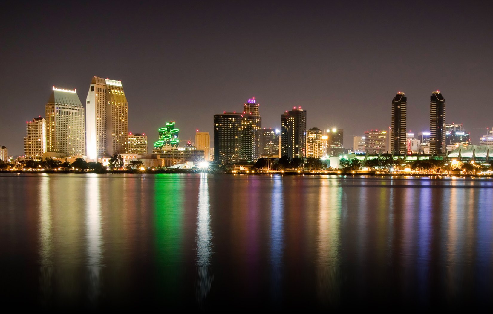 San Diego man-made skyline at night, illuminated high-rises reflected in calm water — HD PC desktop wallpaper/background.