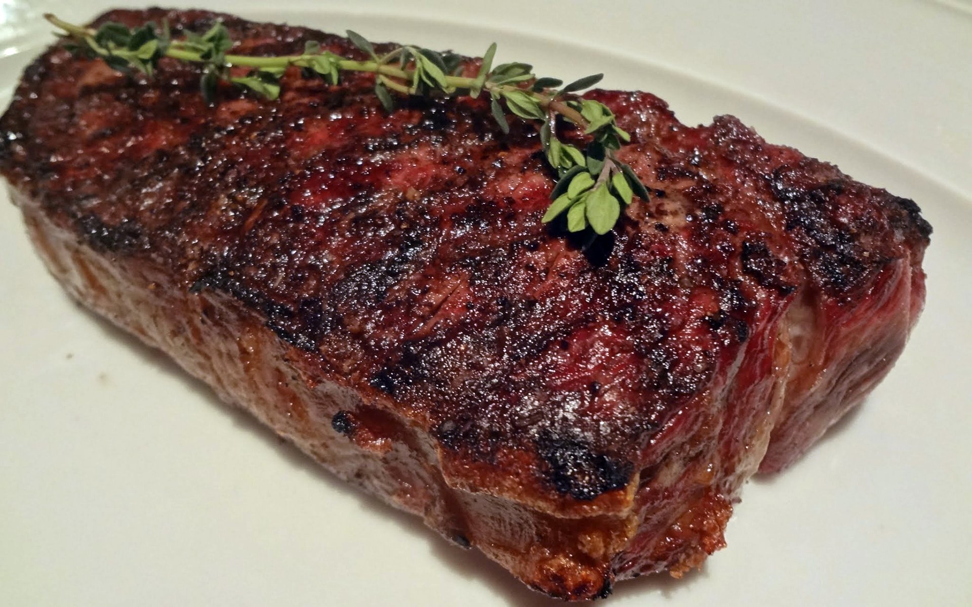 HD PC desktop wallpaper of a grilled steak with charred crust and a sprig of thyme on a white plate — food, meat.
